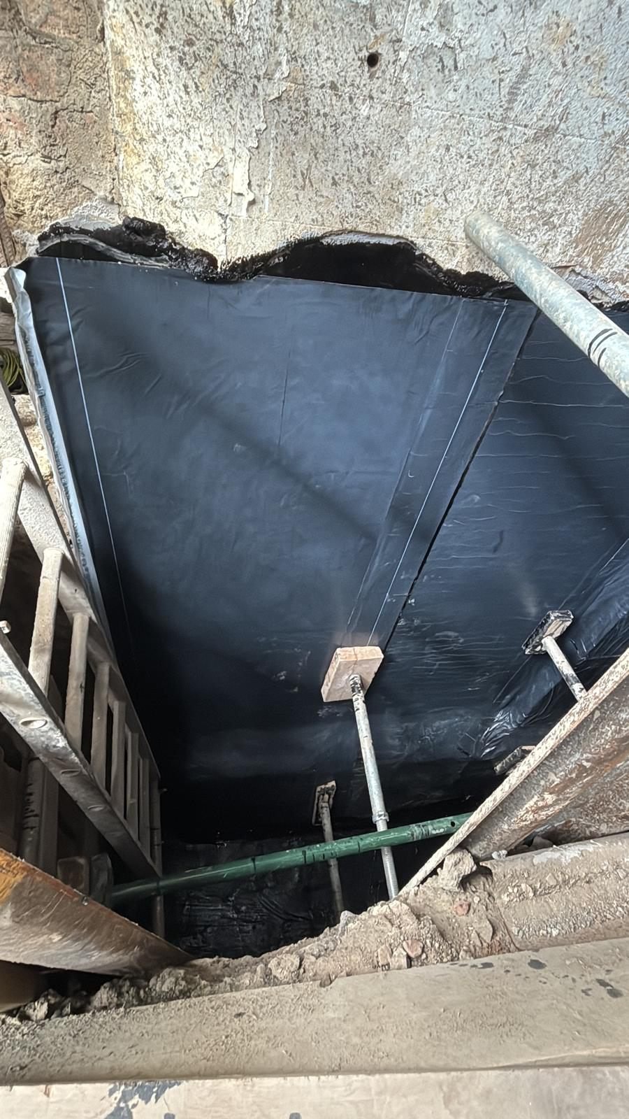 Self-adhesive membrane running down a basement wall and turning onto the floor slab to form a continuous wall-to-floor junction