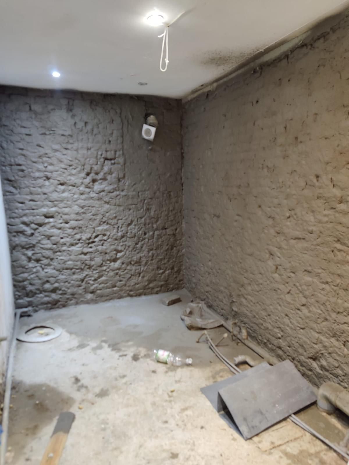 A stripped basement room with walls hacked back and re-rendered, an existing extract vent, and services run around the perimeter of the floor