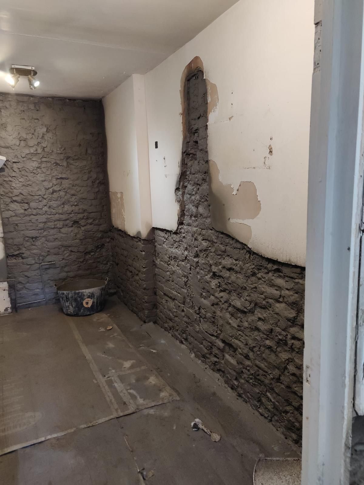 A hallway with the lower wall hacked back to brick and re-rendered to a level line, a vertical chase cut and made good, and the existing floor fully covered with protection boards