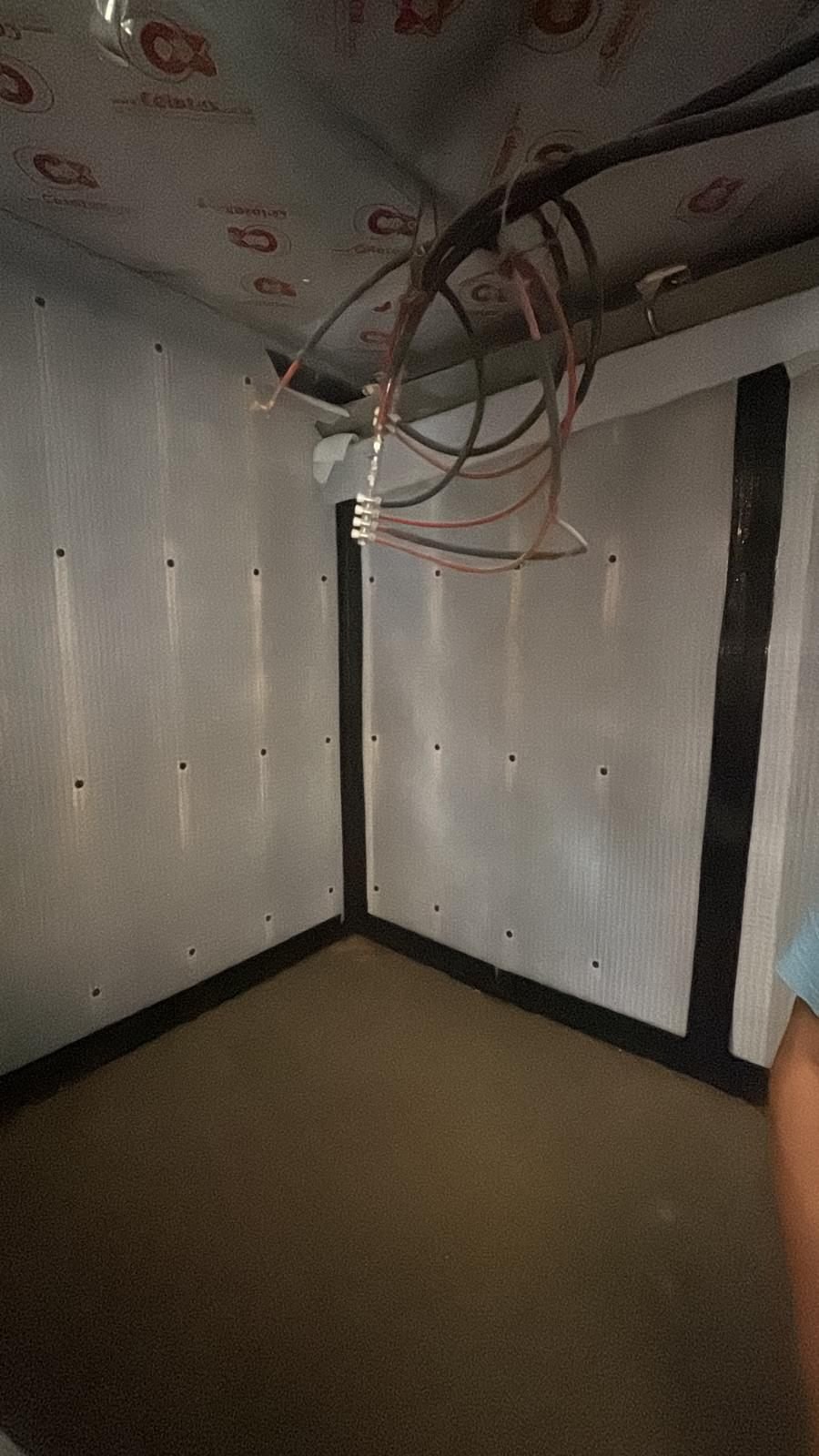 An internal corner of a basement lined with membrane, joints taped at the wall and floor junction, with first-fix electrical cable run clear of the membrane