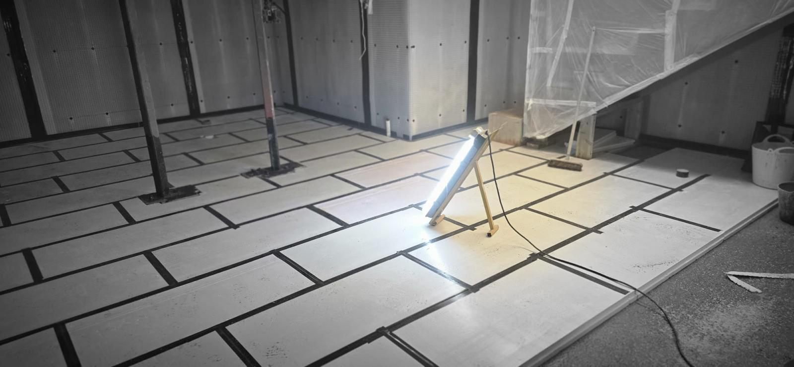 A basement floor of boards laid over a studded membrane in a staggered pattern, every joint taped, with the walls lined out and steel props still standing