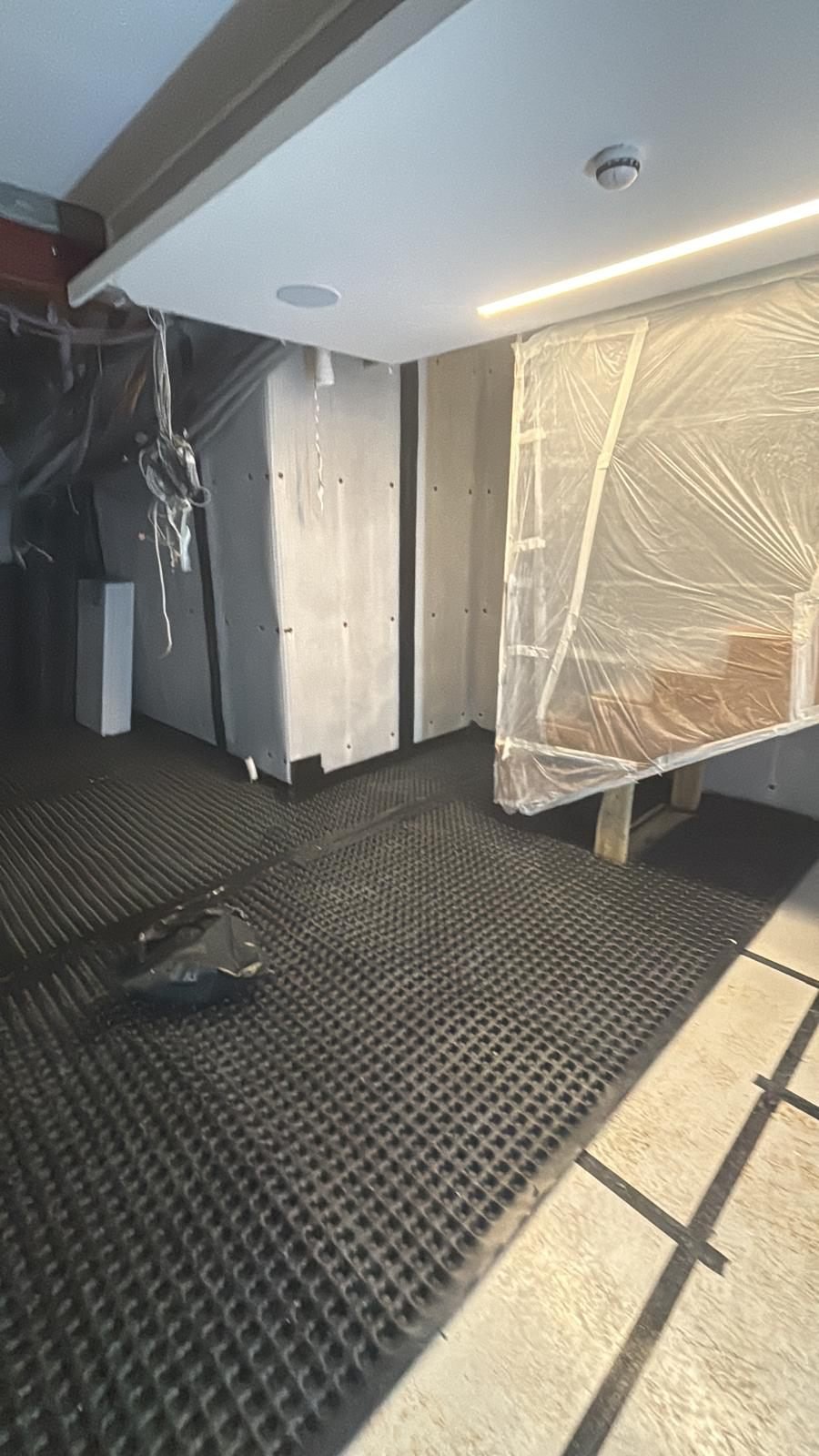 Studded floor membrane being laid across a basement slab up to walls already lined with membrane