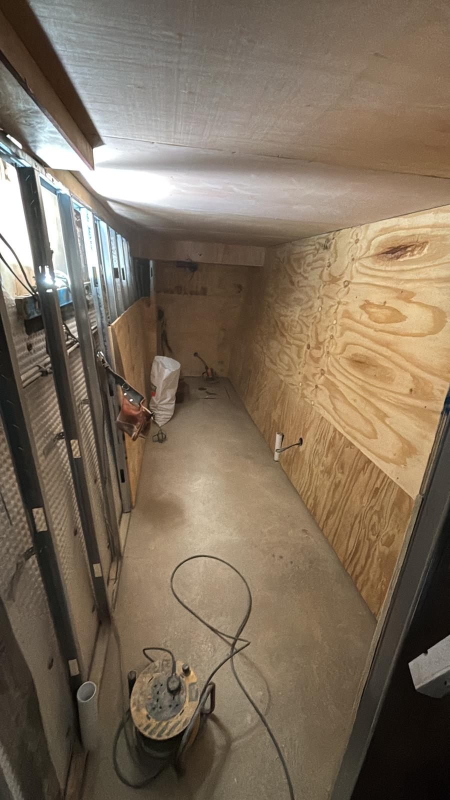 A basement part-lined, with cavity drain membrane and metal framing still visible on one wall and plywood boarding already fixed to the other, over a screeded floor